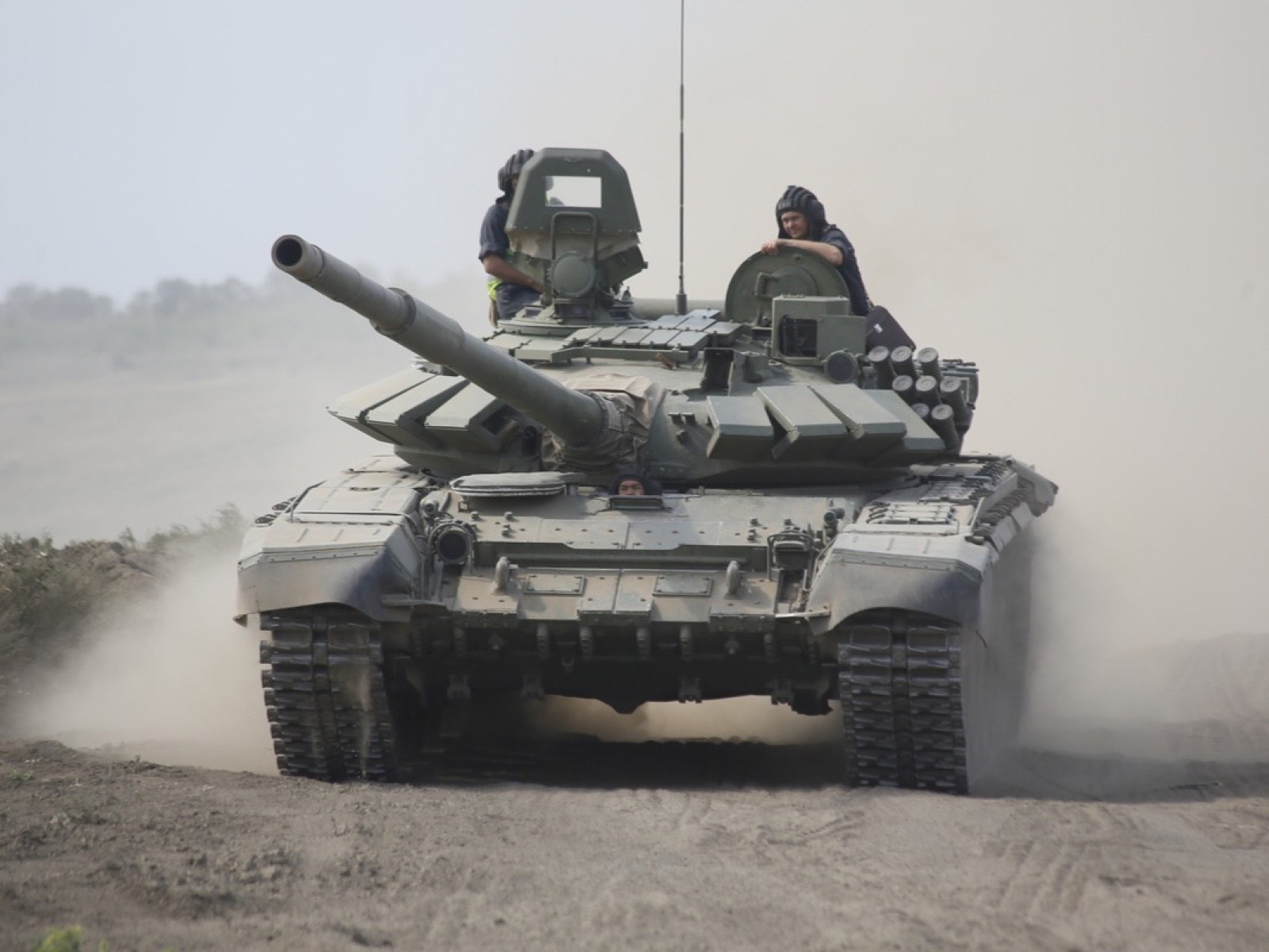 Танк Т-72Б3 с двумя членами экипажа в люках выезжает на полигонную трассу в облаке пыли