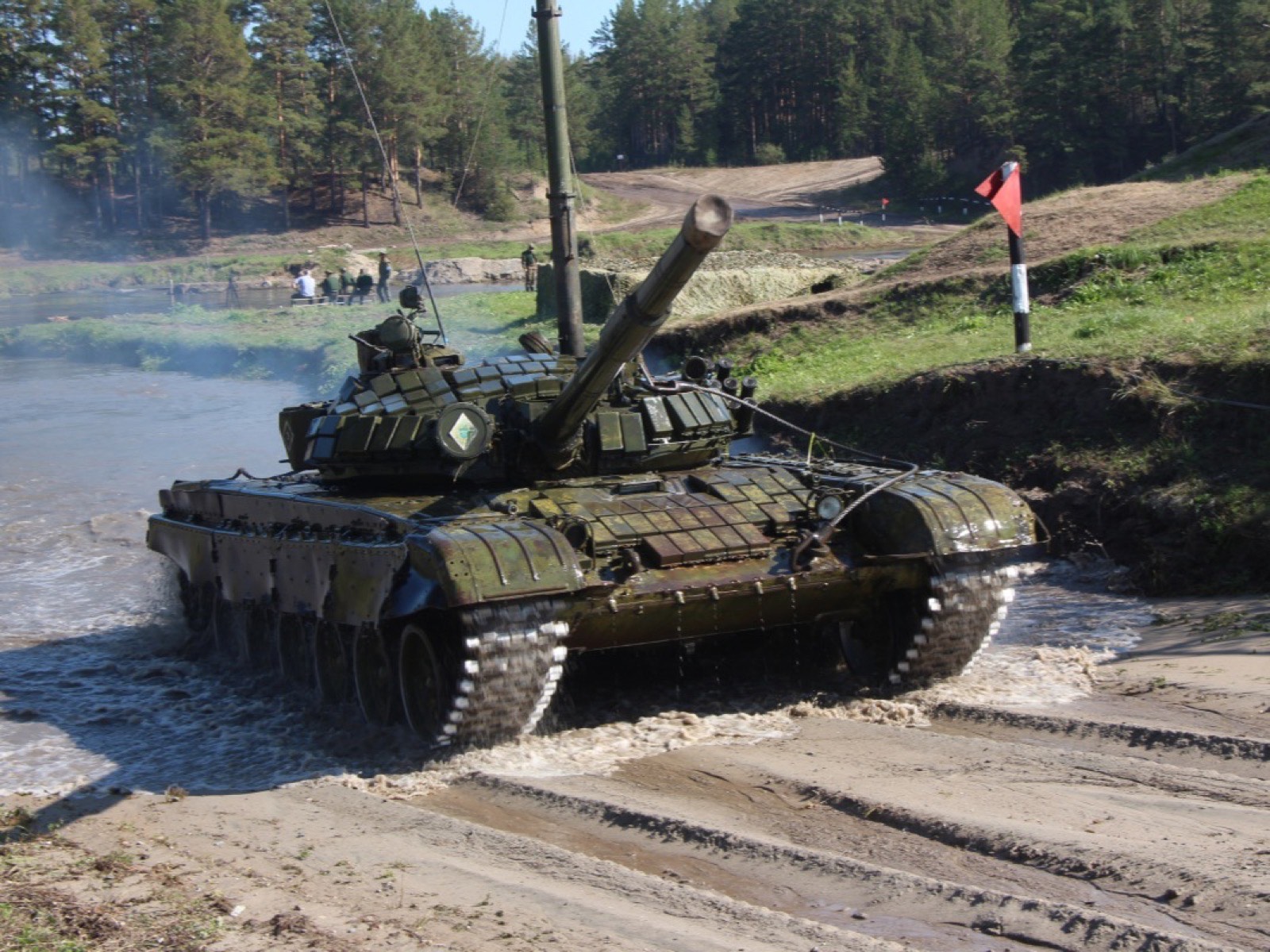 Танк Т-72Б со сноркелем ОПВТ преодолевает водную преграду на полигоне, на берегу у флажка стоят люди